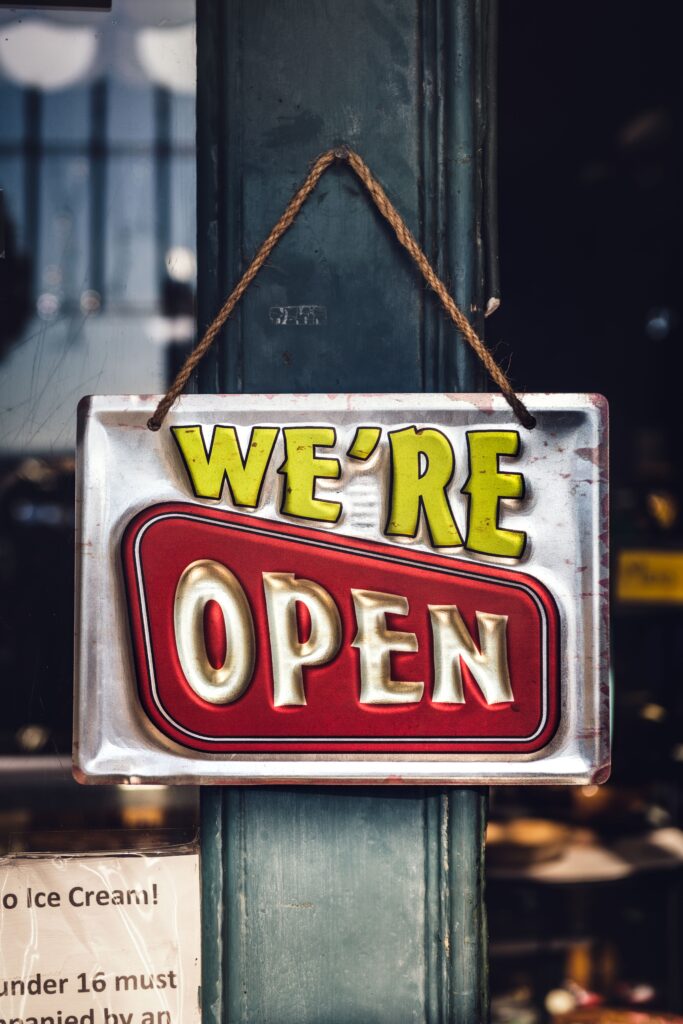 A vintage metal "We're Open" sign hanging by a rope on a shop doorway